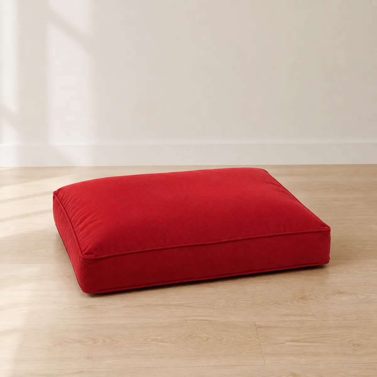 Red rectangular dog bed placed on a light wood floor